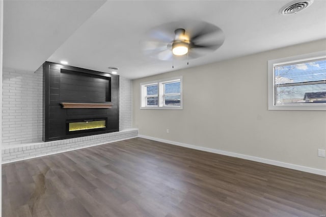 unfurnished living room featuring ceiling fan, a fireplace, wood finished floors, visible vents, and baseboards