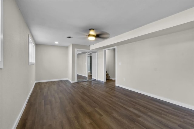 empty room featuring ceiling fan, dark wood-style flooring, visible vents, baseboards, and stairs