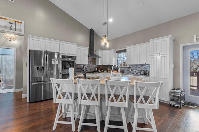 kitchen featuring white cabinets, an island with sink, dark wood-style flooring, stainless steel appliances, and wall chimney range hood