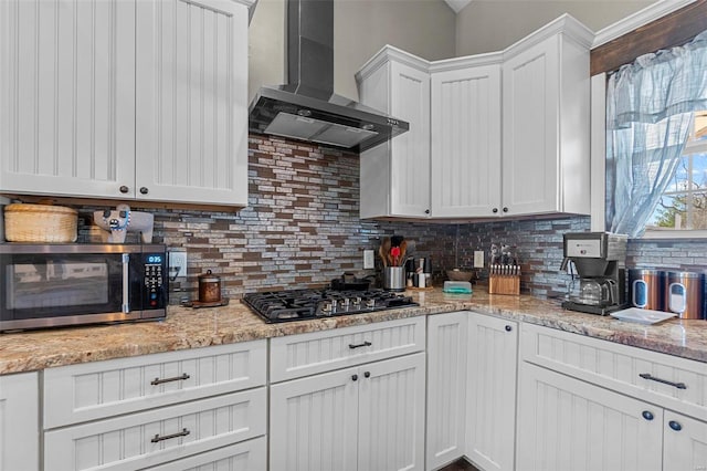 kitchen with decorative backsplash, wall chimney exhaust hood, stainless steel microwave, white cabinetry, and black gas stovetop