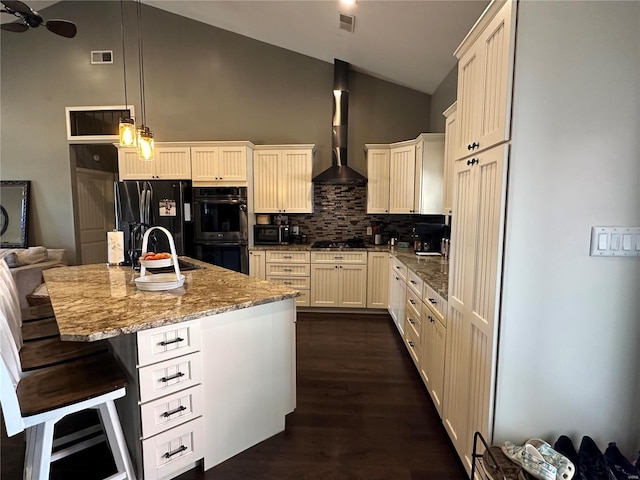 kitchen with double oven, black fridge with ice dispenser, visible vents, light stone countertops, and wall chimney exhaust hood