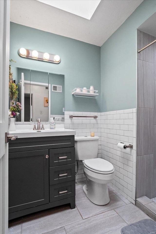 full bath with visible vents, toilet, tile walls, wainscoting, and vanity