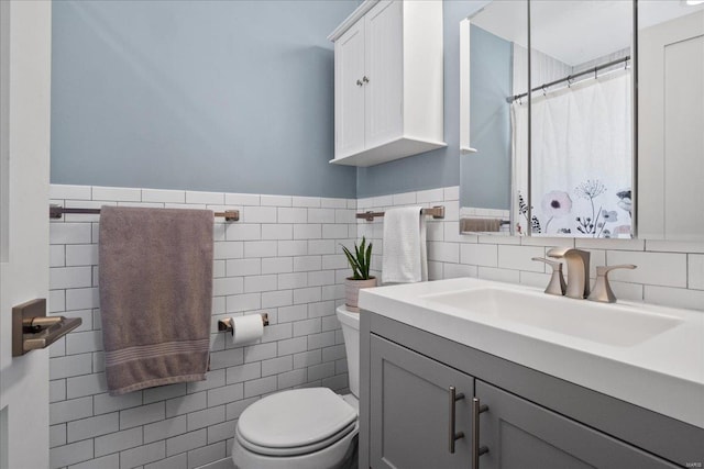 bathroom featuring curtained shower, toilet, vanity, wainscoting, and tile walls