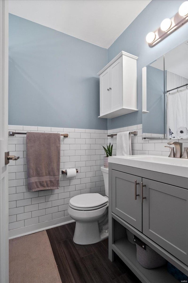 bathroom with toilet, wood finished floors, tile walls, wainscoting, and vanity