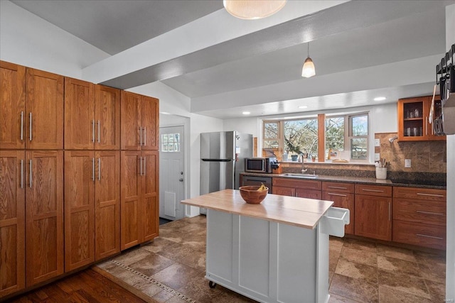 kitchen with brown cabinets, decorative backsplash, a sink, stainless steel appliances, and glass insert cabinets