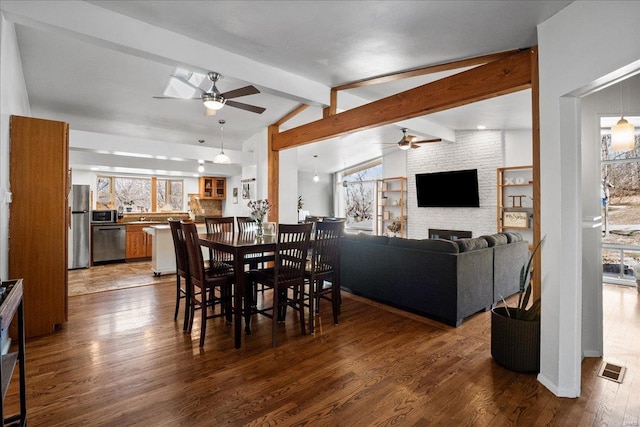 dining space featuring visible vents, ceiling fan, lofted ceiling with beams, a fireplace, and dark wood-style flooring