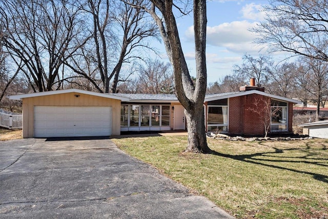 mid-century home featuring driveway, an attached garage, a front yard, brick siding, and a chimney