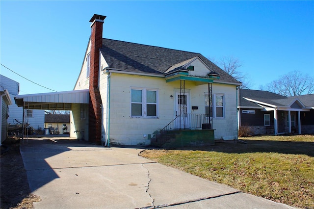 bungalow-style home with a front lawn, an attached carport, concrete driveway, and roof with shingles