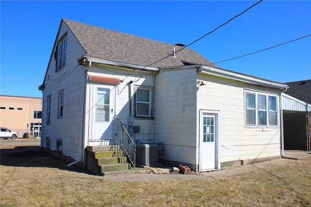 back of house featuring entry steps, a yard, central AC unit, and a shingled roof