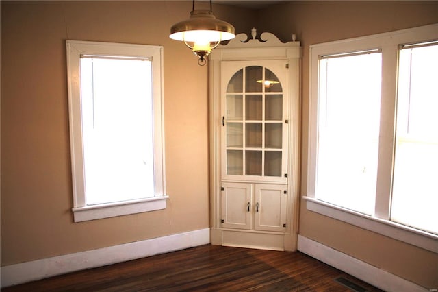 unfurnished dining area featuring dark wood-style floors, visible vents, and baseboards