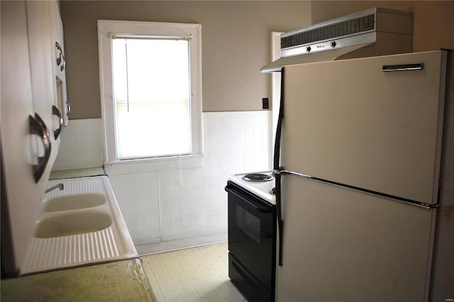 kitchen featuring electric range, a wainscoted wall, freestanding refrigerator, tile walls, and exhaust hood