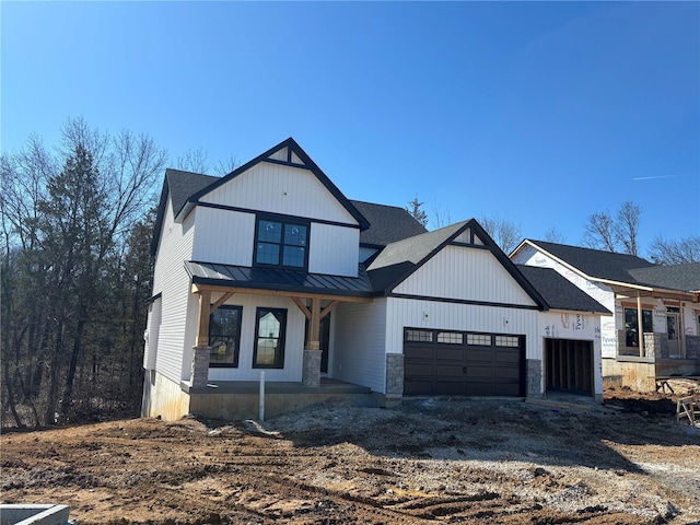 modern farmhouse style home featuring dirt driveway, a standing seam roof, metal roof, a garage, and stone siding