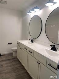 bathroom featuring a sink, double vanity, wood finished floors, and toilet