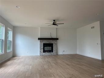 unfurnished living room with a ceiling fan, visible vents, a stone fireplace, and light wood finished floors