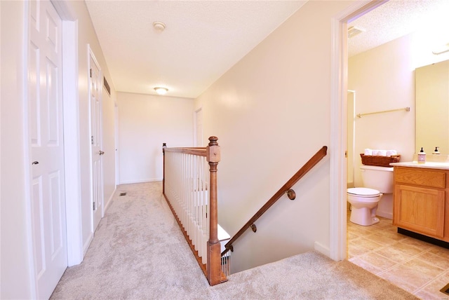 hall featuring light colored carpet, a textured ceiling, and an upstairs landing