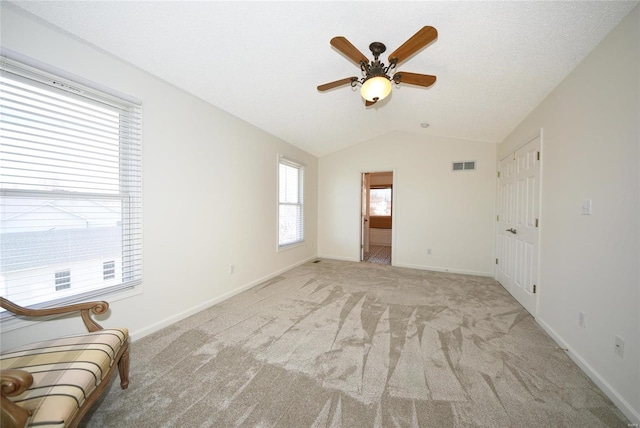 interior space featuring light colored carpet, visible vents, lofted ceiling, and baseboards