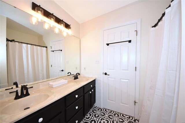 bathroom featuring a wainscoted wall, double vanity, a sink, and tile walls