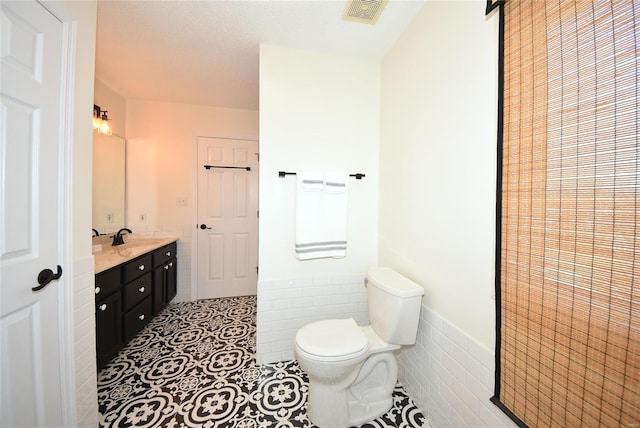 bathroom featuring tile patterned flooring, toilet, visible vents, tile walls, and wainscoting