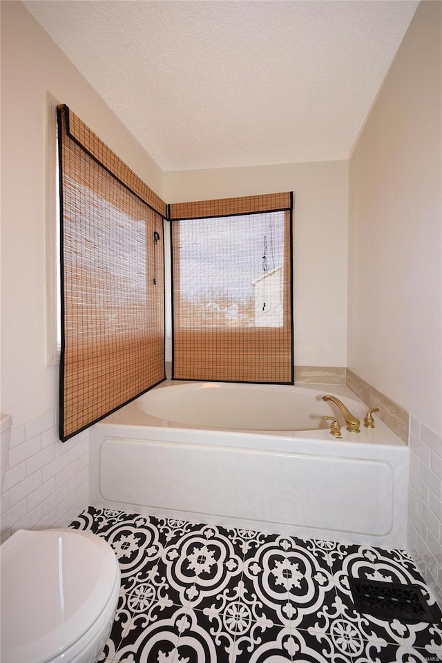 full bathroom featuring a textured ceiling, a tub to relax in, toilet, tile walls, and tile patterned floors