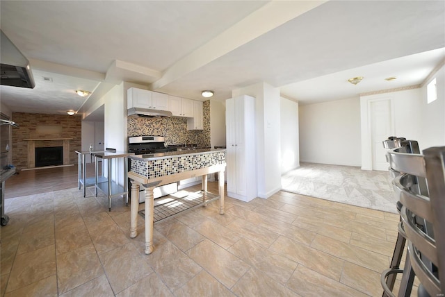 kitchen with a fireplace, tasteful backsplash, open floor plan, white cabinetry, and gas range