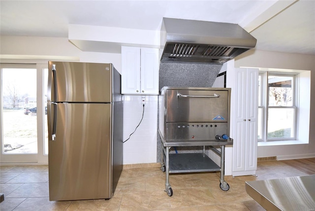 kitchen with oven, exhaust hood, freestanding refrigerator, and white cabinets