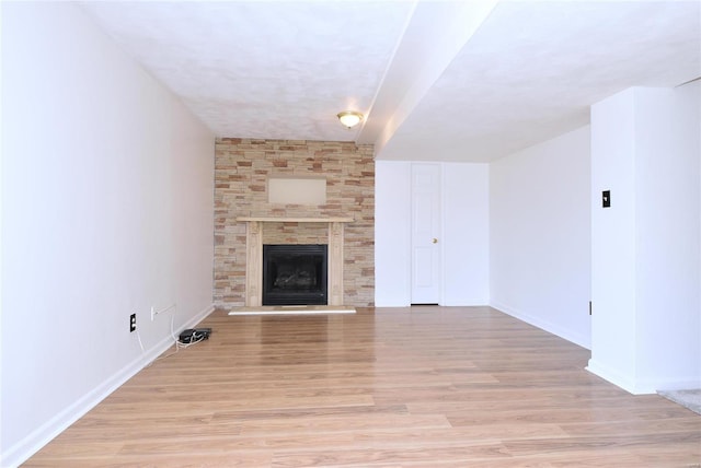 unfurnished living room with light wood finished floors, baseboards, and a stone fireplace