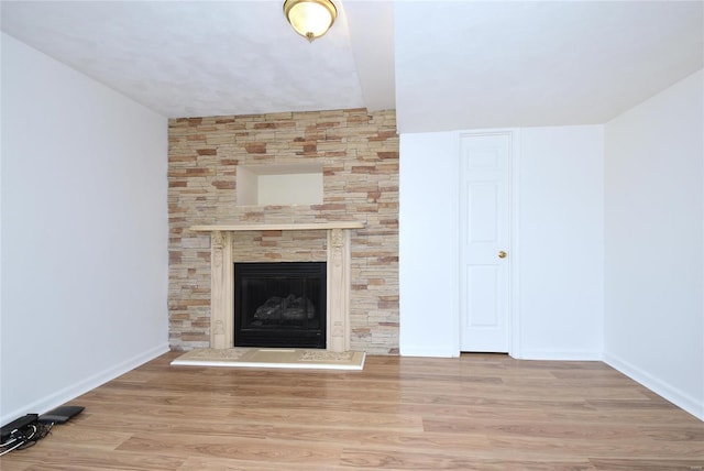 unfurnished living room with baseboards, a fireplace with raised hearth, and wood finished floors