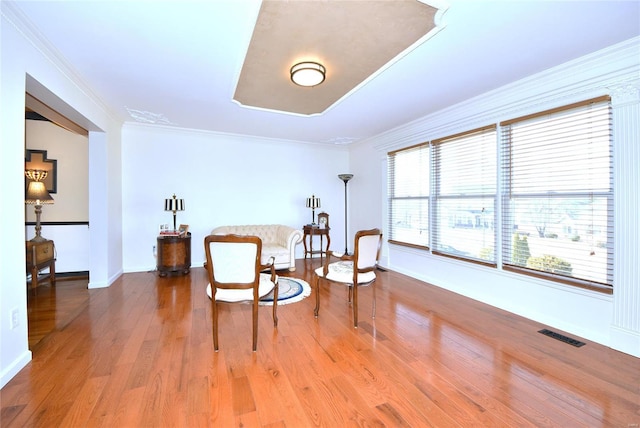 living area featuring visible vents, crown molding, baseboards, and wood finished floors