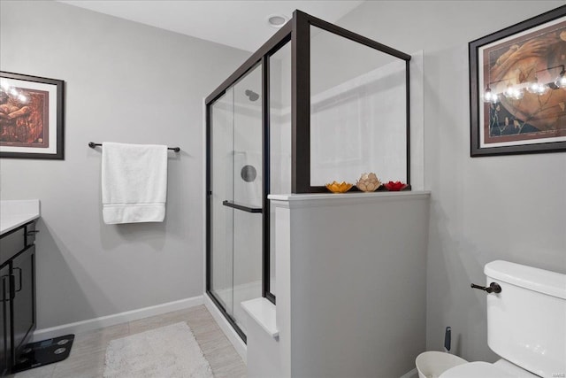 bathroom with toilet, a shower stall, vanity, and baseboards