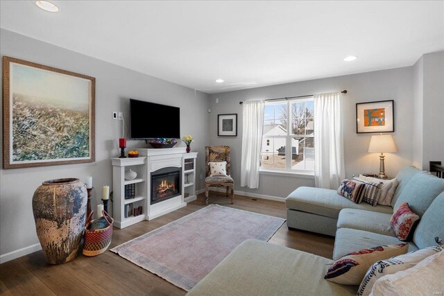 living room featuring a glass covered fireplace, recessed lighting, baseboards, and wood finished floors