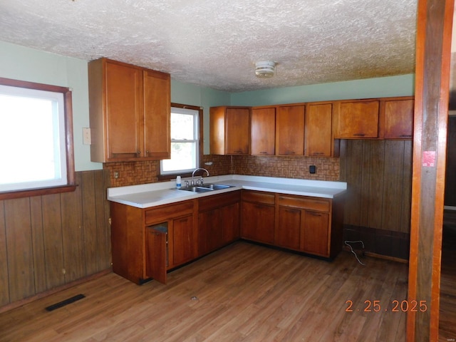 kitchen featuring light wood-style floors, visible vents, brown cabinets, and a sink