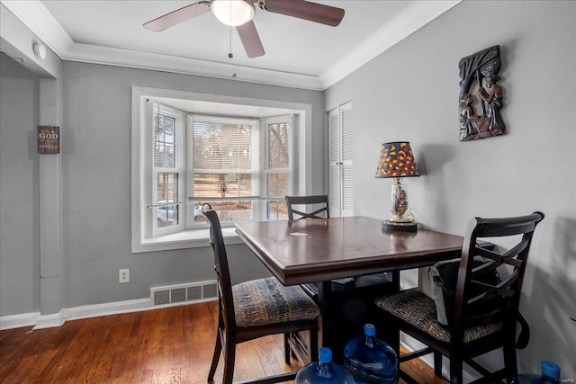 dining space featuring baseboards, wood finished floors, visible vents, and crown molding