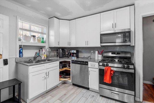 kitchen featuring light wood finished floors, decorative backsplash, appliances with stainless steel finishes, white cabinetry, and a sink