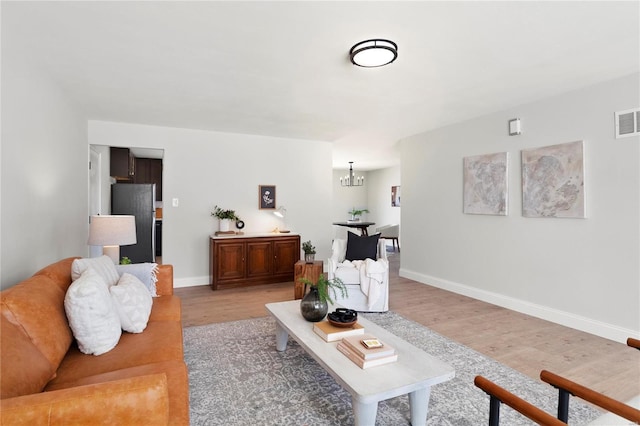 living area with a chandelier, visible vents, light wood finished floors, and baseboards