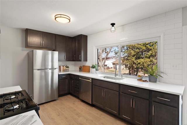 kitchen featuring light wood-type flooring, a sink, appliances with stainless steel finishes, light countertops, and dark brown cabinets