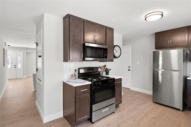 kitchen with dark brown cabinetry, light countertops, decorative backsplash, light wood-style flooring, and stainless steel appliances