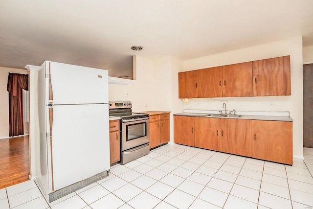 kitchen with light tile patterned floors, a sink, light countertops, freestanding refrigerator, and stainless steel range with electric stovetop