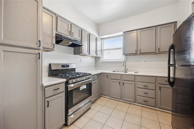 kitchen featuring gray cabinetry, under cabinet range hood, a sink, stainless steel range with gas cooktop, and freestanding refrigerator