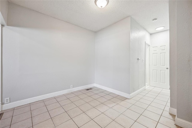 empty room featuring light tile patterned floors, baseboards, and a textured ceiling