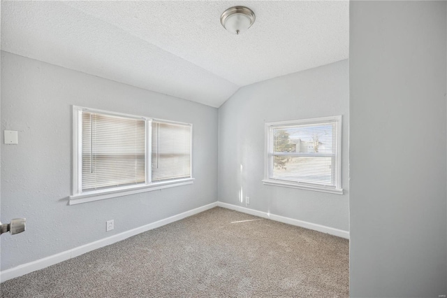 carpeted spare room featuring a textured ceiling, vaulted ceiling, and baseboards