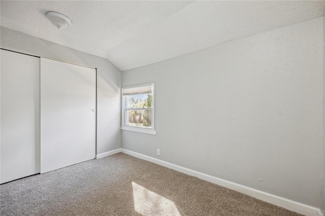 unfurnished bedroom with a textured ceiling, lofted ceiling, carpet flooring, baseboards, and a closet