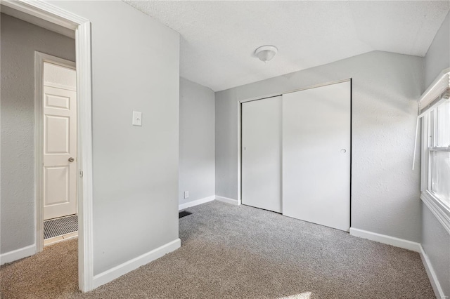 unfurnished bedroom with lofted ceiling, a closet, carpet flooring, a textured ceiling, and baseboards