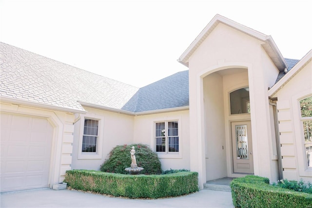 property entrance featuring an attached garage, roof with shingles, and stucco siding