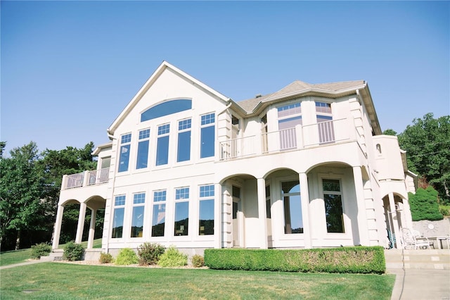 view of front of home featuring a front lawn, a balcony, and stucco siding