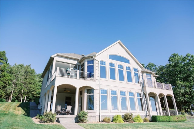 rear view of property featuring a patio, a balcony, a ceiling fan, a lawn, and stucco siding