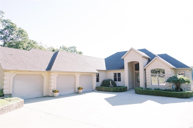 ranch-style house featuring a shingled roof, driveway, an attached garage, and stucco siding