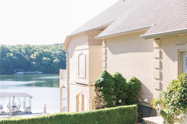 exterior space with a water view, roof with shingles, and stucco siding