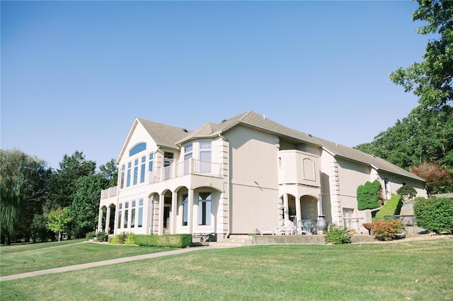 view of front of home featuring a balcony, stucco siding, and a front yard