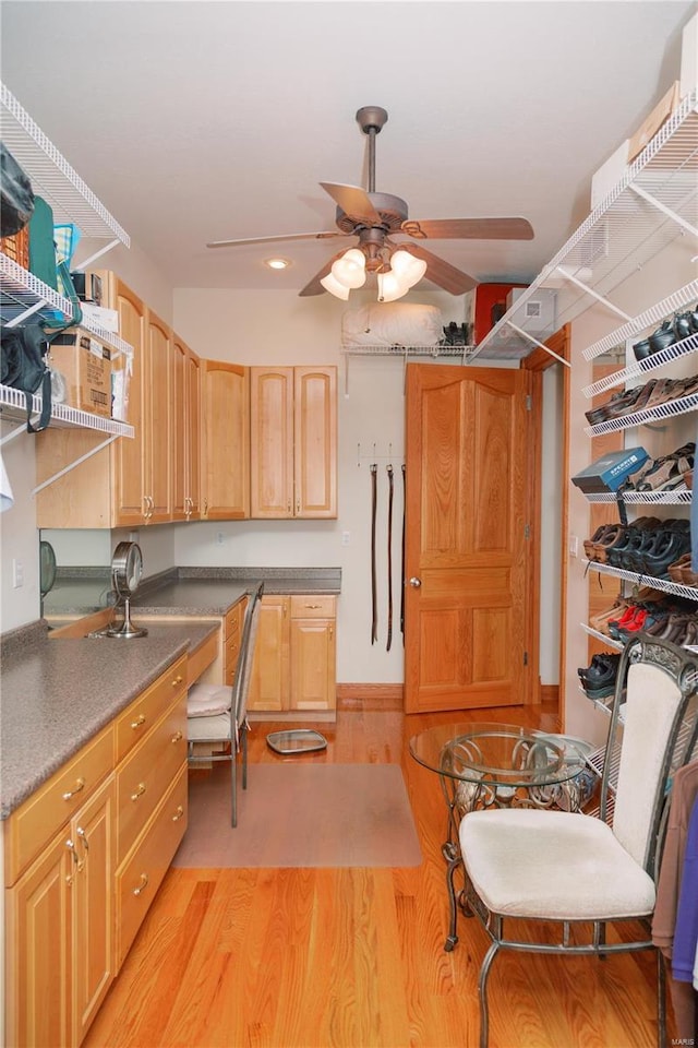 kitchen featuring light brown cabinetry, built in desk, light wood-type flooring, and a ceiling fan