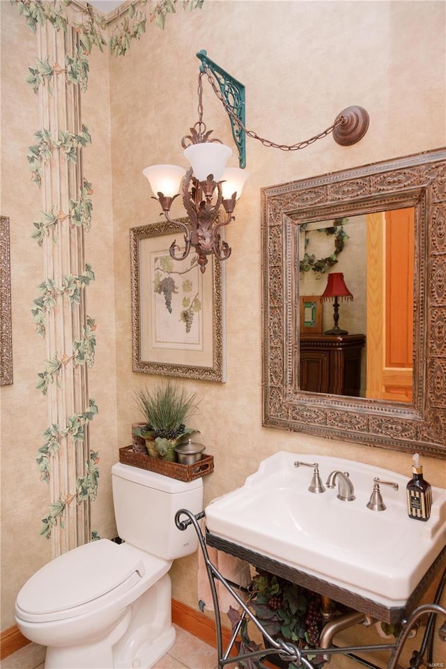 half bathroom with baseboards, toilet, tile patterned flooring, a chandelier, and a sink